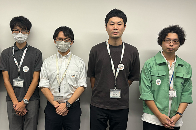 Four individuals standing side by side wearing ID badges and casual or business-casual attire.