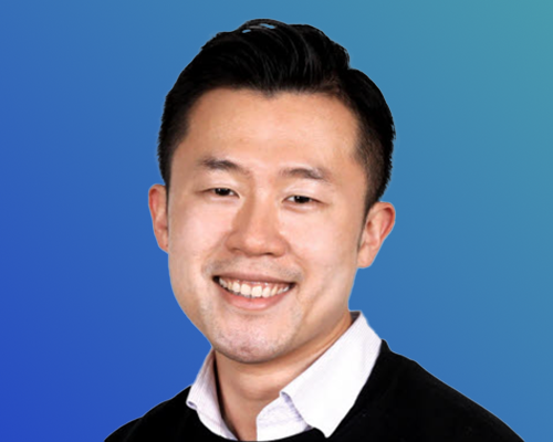 A person wearing a white collared shirt and black sweater against a blue gradient background.