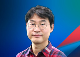 A man with glasses and short hair wearing a red plaid shirt, posed in front of a blue gradient background with a red and blue geometric accent.