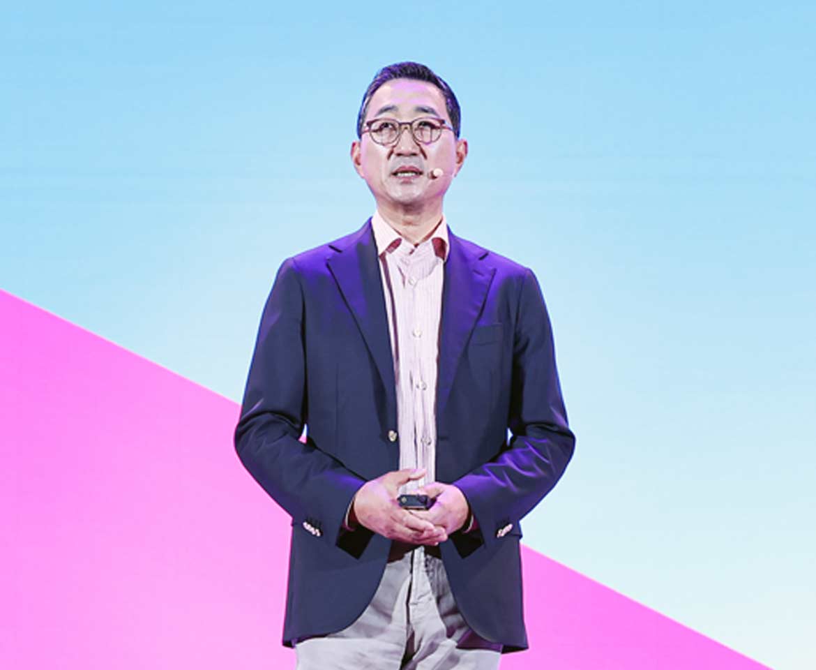 A person wearing a navy blazer and light pink shirt stands against a vibrant background of blue and pink diagonal colors.