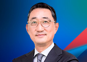 A business professional wearing glasses and a suit, posing against a blue and red abstract background.