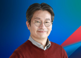 A person wearing glasses and a red sweater is smiling in front of a blue and green gradient background with a red geometric accent.