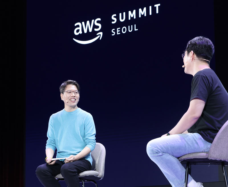 Two people seated on stage at the AWS Summit Seoul, with one speaking into a microphone.