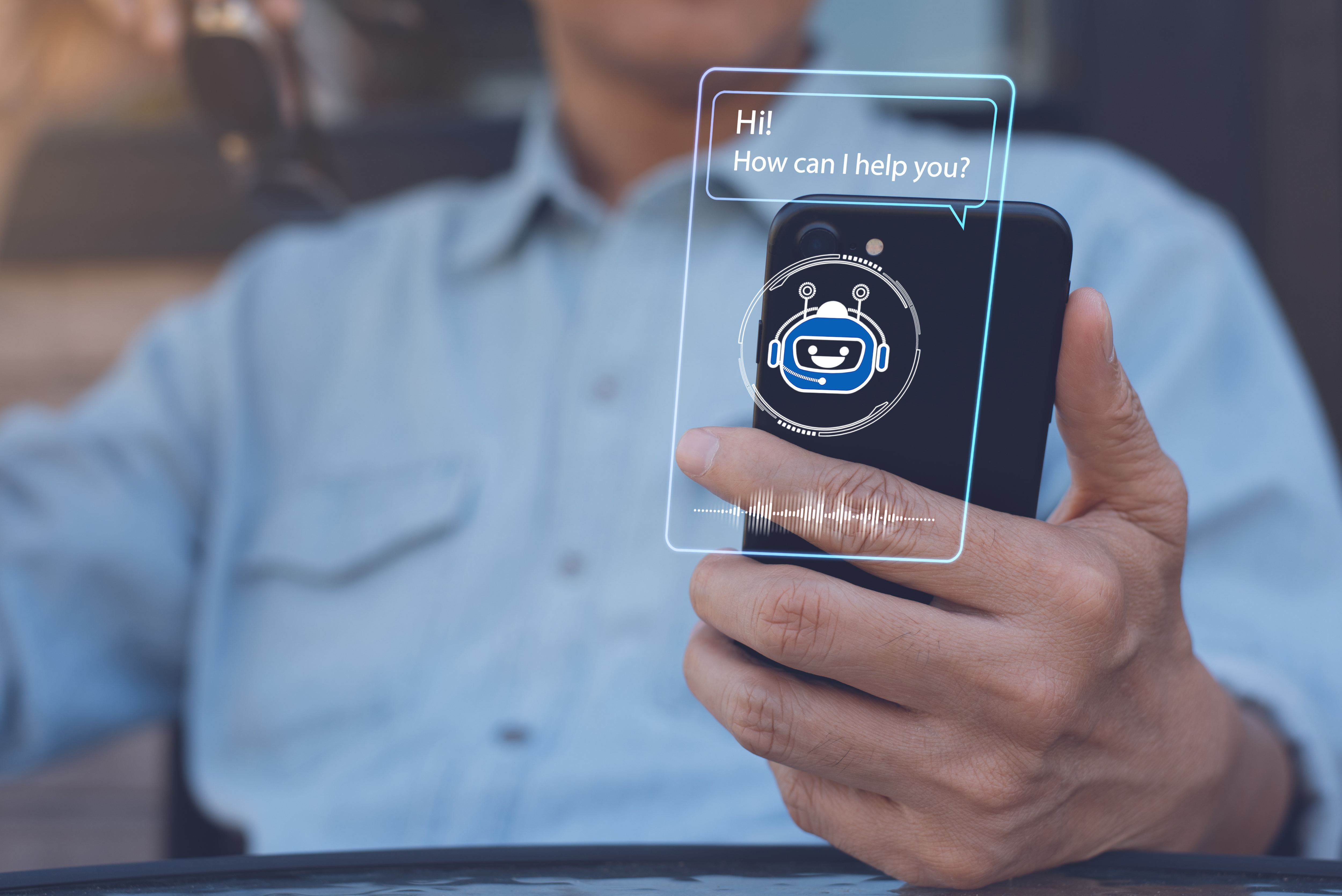 Person holding a smartphone with a digital chatbot assistant interface displayed, showing a friendly robot icon and the message 'Hi! How can I help you?'. Represents AI communication and customer service via mobile device.