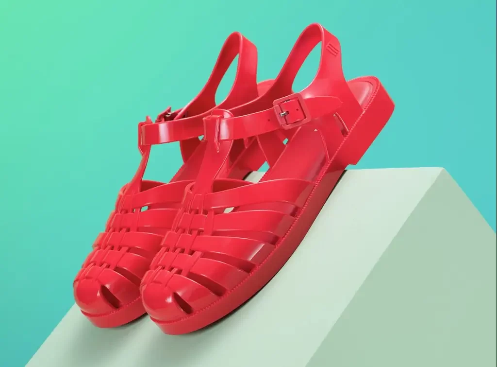 A pair of bright red Grendene Melissa sandals displayed on a light geometric surface with a blue-green background.