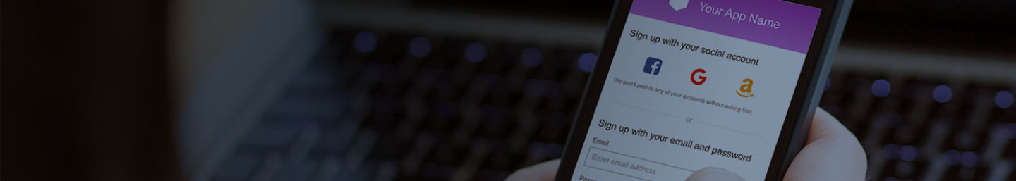 A person holding a smartphone displaying a signup screen for a mobile app, showing options to sign up using social accounts such as Facebook, Google, and Amazon, or with email and password. A laptop keyboard is visible in the background.
