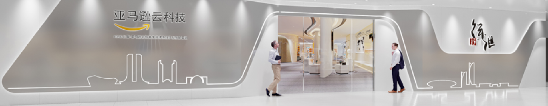 Entrance view of the AWS China Cloud Technology Exhibition Hall, featuring a modern, illuminated facade with two people walking toward the glass entry, AWS branding, and Chinese characters on the wall.