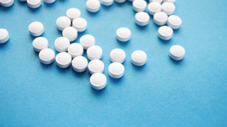 A collection of white round pills scattered on a blue background, representing pharmaceutical drug discovery with quantum computing technology.