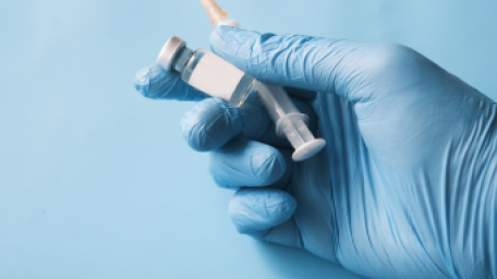 A gloved hand holding a vaccine vial and syringe against a blue background.