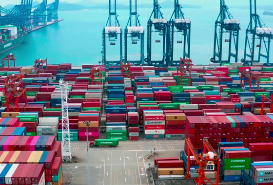 A busy shipping port with stacks of colorful cargo containers and large cranes by the water.