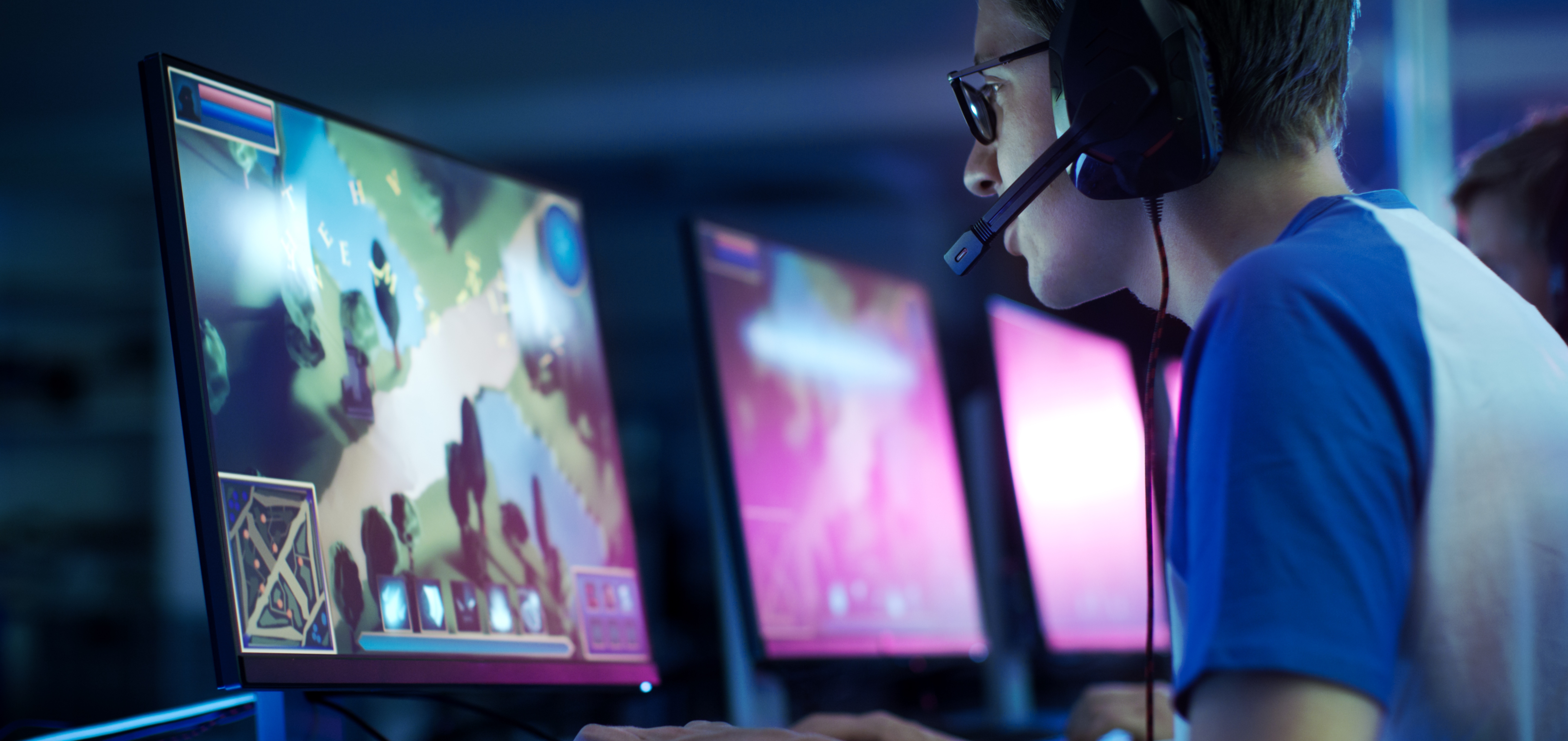 A person wearing headphones playing a colorful video game on a computer monitor in a dimly lit room.