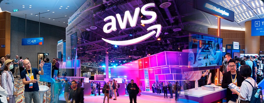 A vibrant scene from an AWS Summit expo booth event, featuring attendees interacting, informational booths, and a large illuminated AWS logo at the center of the exhibition space.