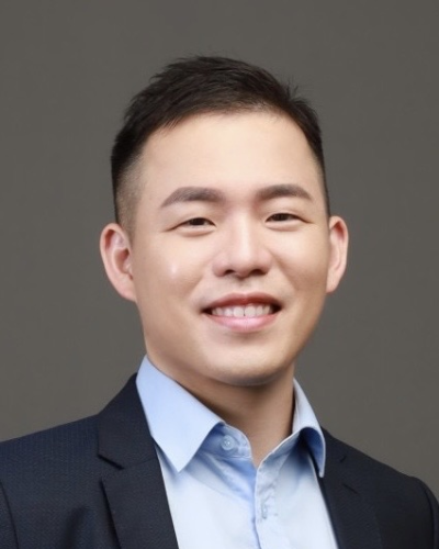 Business portrait of a smiling man wearing a suit and blue shirt, posing against a plain background.