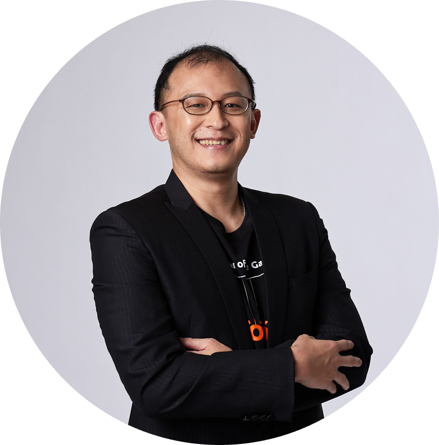 A person wearing a black suit and a black shirt with folded arms, standing against a plain white background.