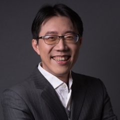 Professional portrait of a smiling man in a suit with glasses against a dark background