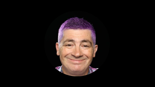 A smiling man with purple hair, shown against a solid black background.