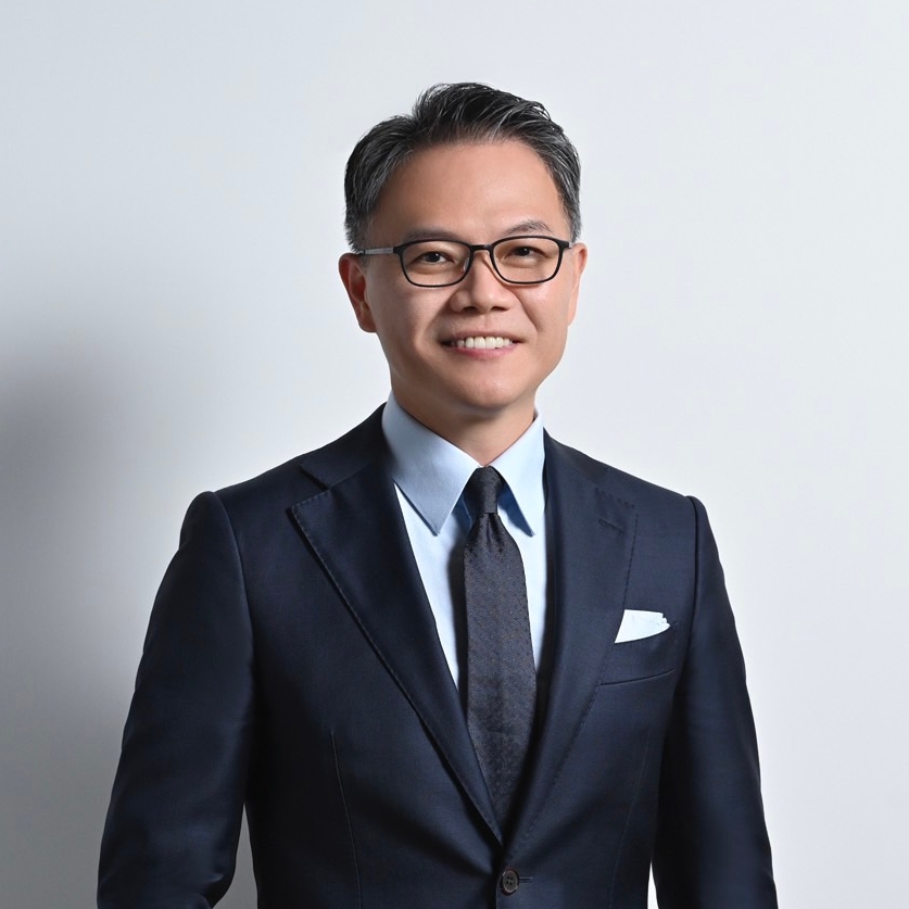 Portrait of a business professional man wearing a suit, tie, and glasses, standing against a plain background.