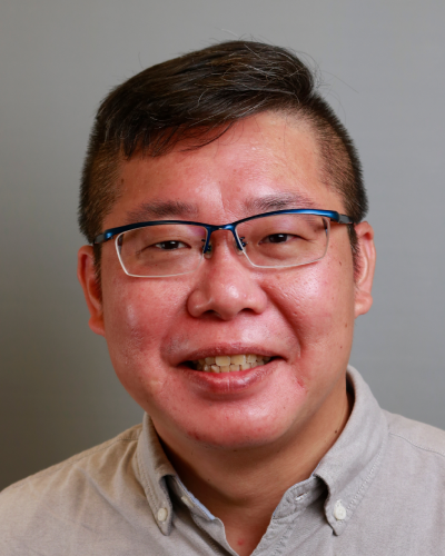Portrait of a man with glasses smiling, wearing a light-colored collared shirt, with a neutral background.