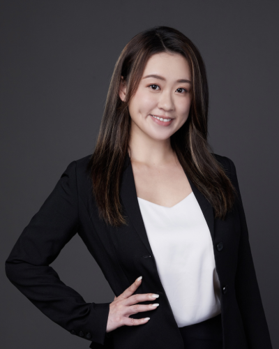 Professional portrait of a woman wearing a black suit and white top, posing confidently against a dark background.
