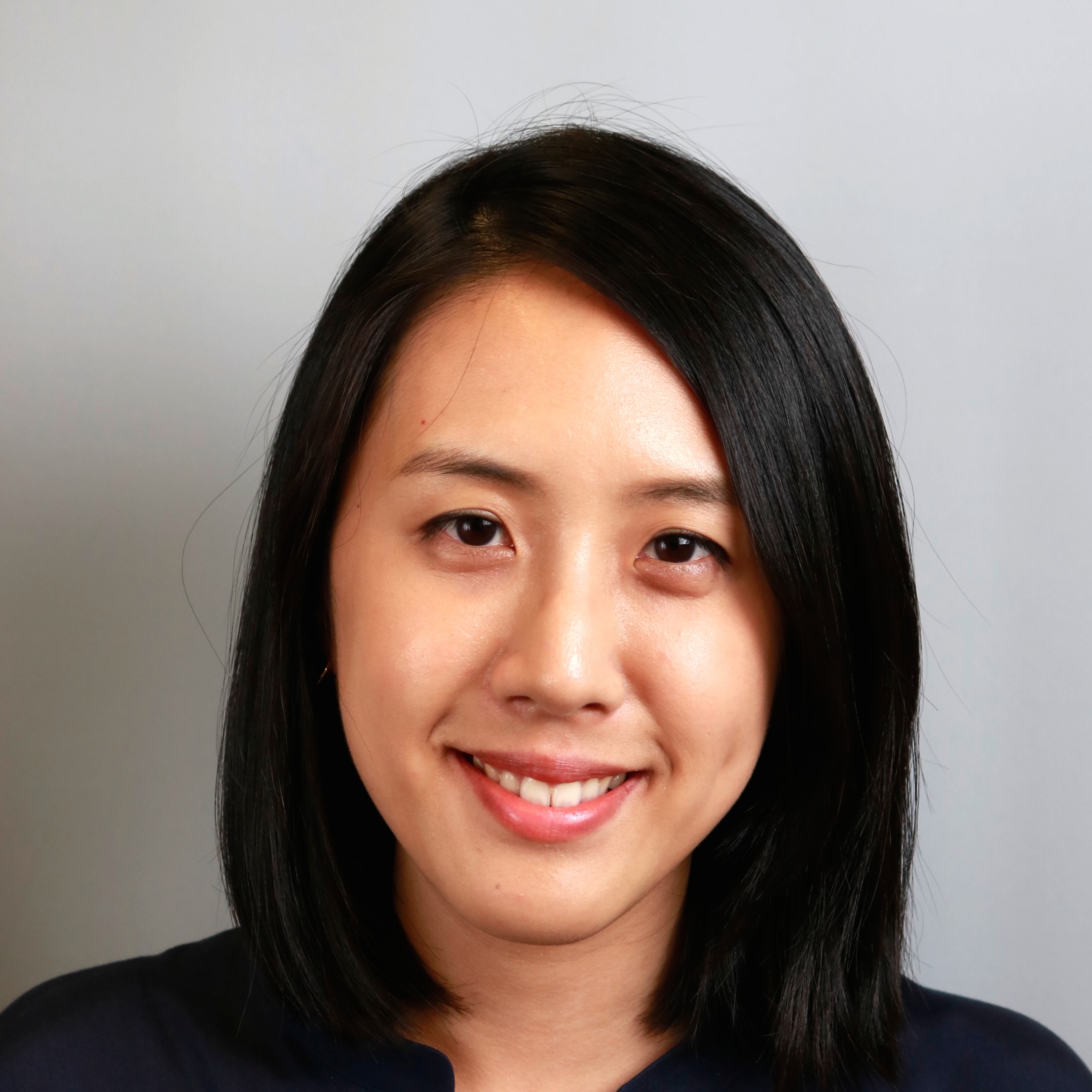 Professional headshot of Jenn Yeh, showing a woman with straight black hair, wearing a dark top, and smiling in front of a plain background.