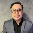 Portrait of a man wearing a gray blazer and glasses against a neutral background.