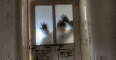 A blurry human figure with raised hands is visible behind a frosted glass door. The scene is atmospheric and slightly eerie, showing only the silhouette and outstretched hands through the translucent glass.
