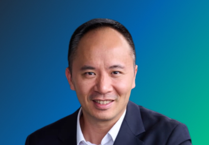 A person in a suit against a gradient blue and green background.