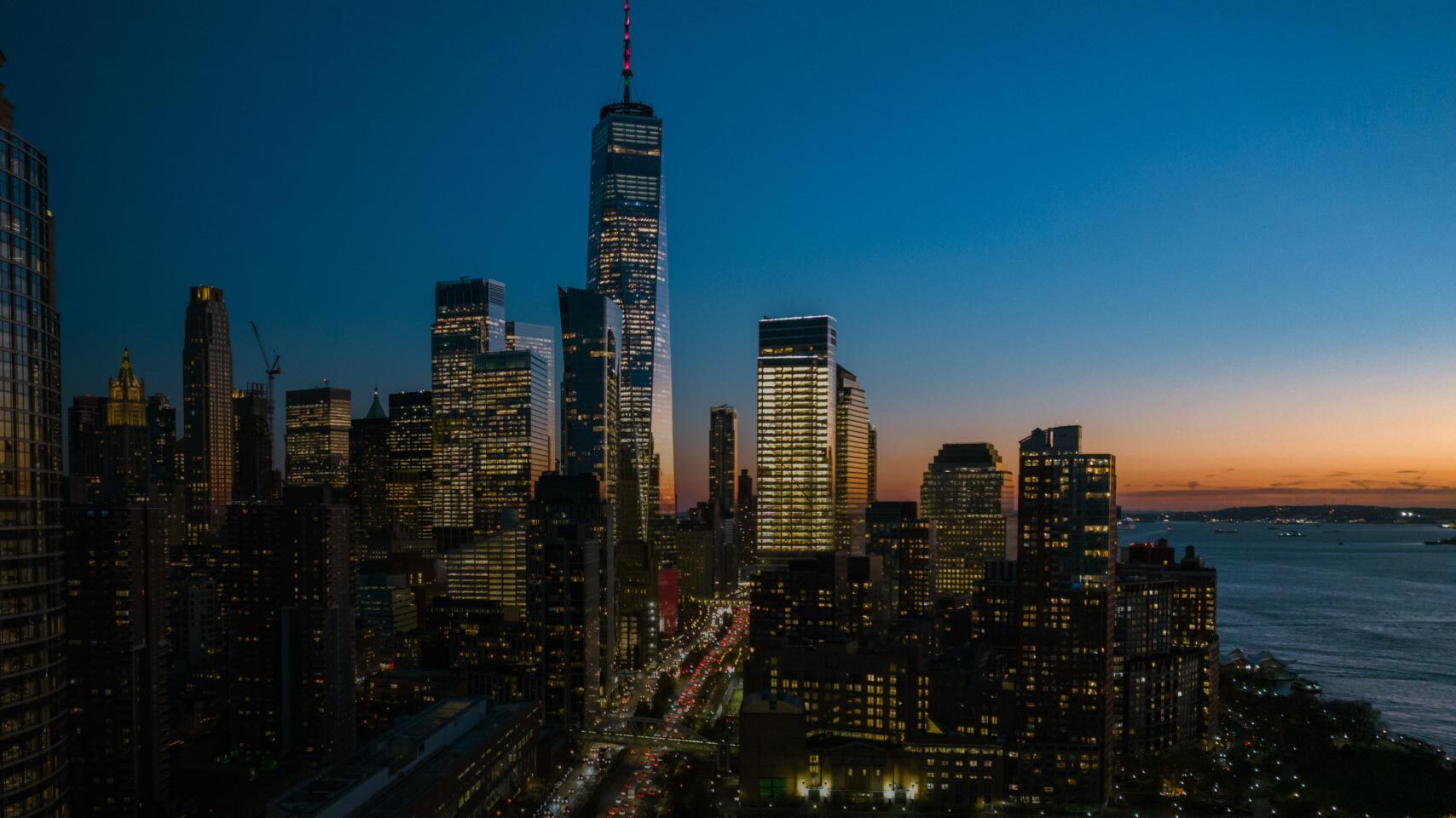A city skyline at dusk with illuminated skyscrapers and an ocean horizon, representing high performance computing (HPC) and generative AI technology, in reference to AWS EC2 P5 instance launch.