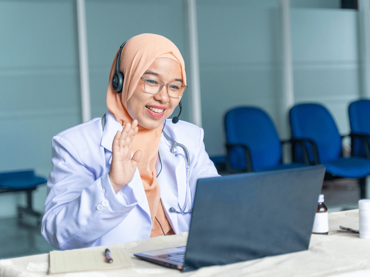 Woman with headset waving at laptop representing AWS media solutions for streaming and video communication