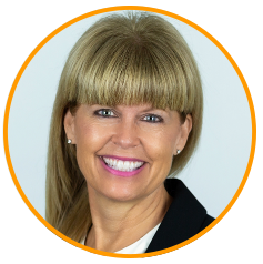 A person with straight blonde hair wearing a black blazer and white shirt, framed by an orange circle.