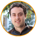 A person outdoors with trees and a building in the background, framed by an orange circle.