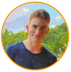 A person wearing a dark shirt standing outdoors with a scenic background of trees, streetlights, and distant mountains.