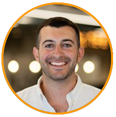 A professional headshot portrait of a smiling person in business casual attire, shown in front of a blurred background with circular lights.