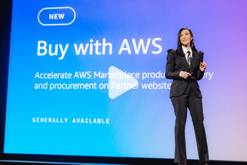 A presenter in formal attire stands on stage in front of a screen displaying "Buy with AWS" and information about accelerating AWS Marketplace procurement, with "Generally Available" noted below.