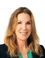 Professional headshot of a woman with long blonde hair, wearing a black blazer and green blouse, smiling against a white background.