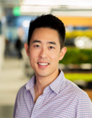 A person is smiling and posed in front of an office background with blurred details.