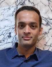 Portrait of an individual in a blue shirt in front of a marble background.