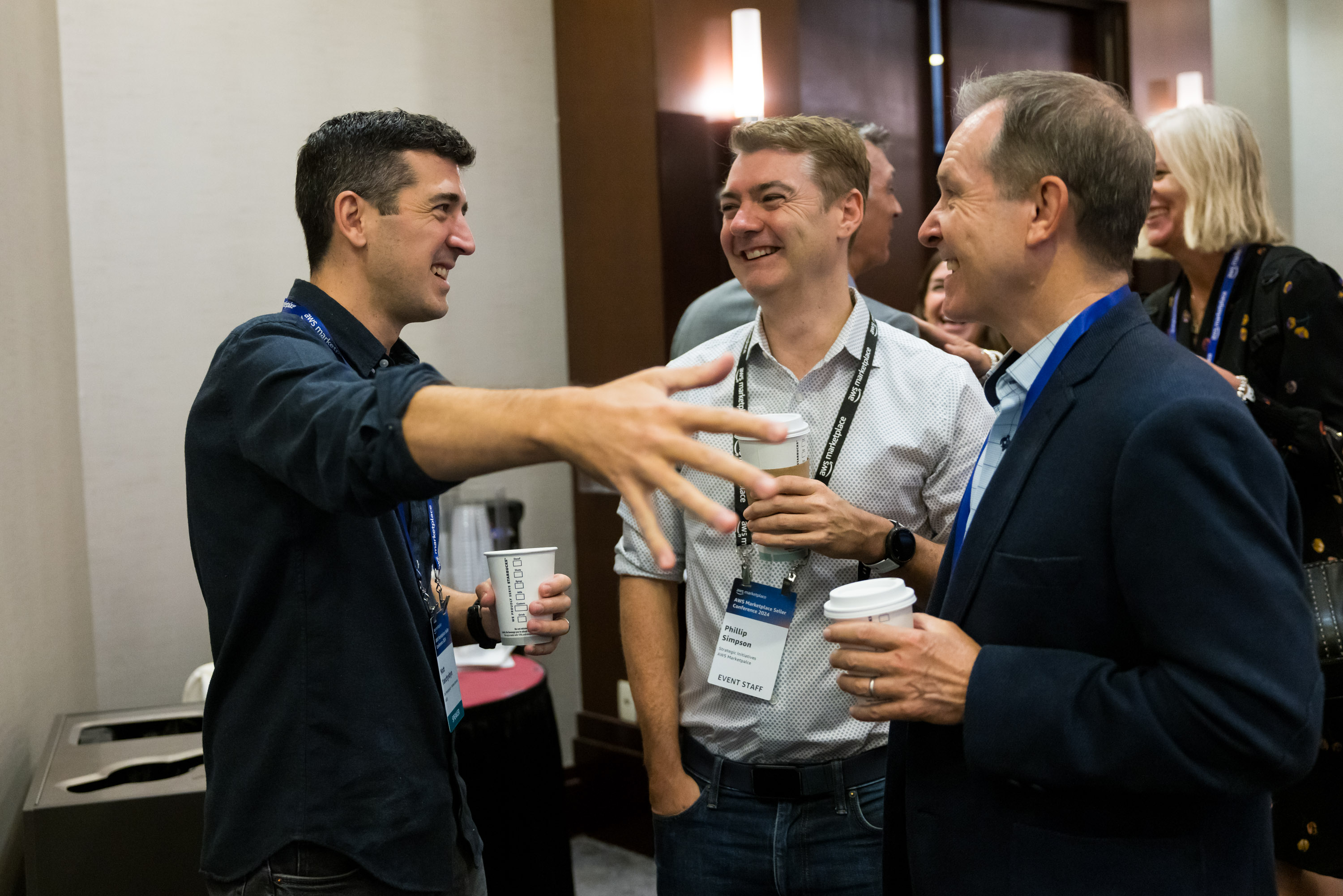 A group of people engaging in a lively conversation during the welcome reception at the AWS Marketplace 2024 Seller Conference. Participants appear to be networking, holding coffee cups, and wearing event badges in a conference setting.
