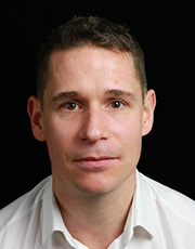 A portrait headshot of an individual wearing a white shirt, set against a black background.