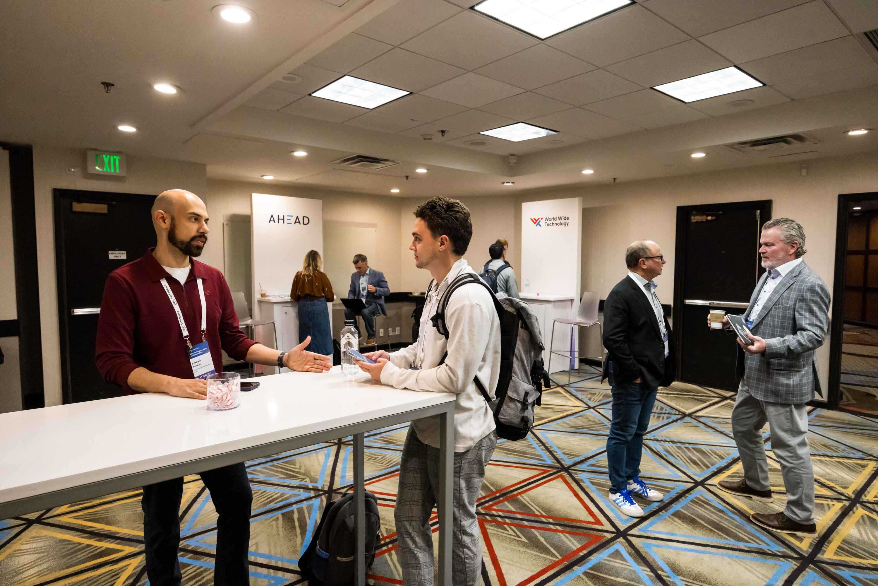 Attendees networking and having conversations in a lounge area at the AWS Marketplace 2024 conference, with branded booths in the background.