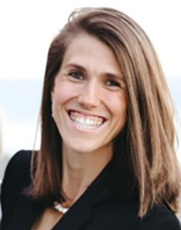 Portrait of a smiling woman with straight brown hair, wearing business attire and a necklace, in front of a bright background.