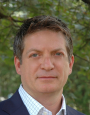 Portrait of a business professional in a suit, standing outdoors with a background of greenery.