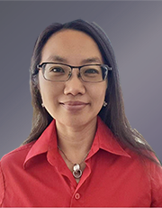 Portrait of a woman wearing glasses and a red shirt, with long dark hair, in front of a gray background.