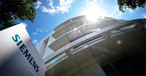 A modern Siemens building captured from a low angle with sunlight shining above, highlighting contemporary architecture and the Siemens sign.