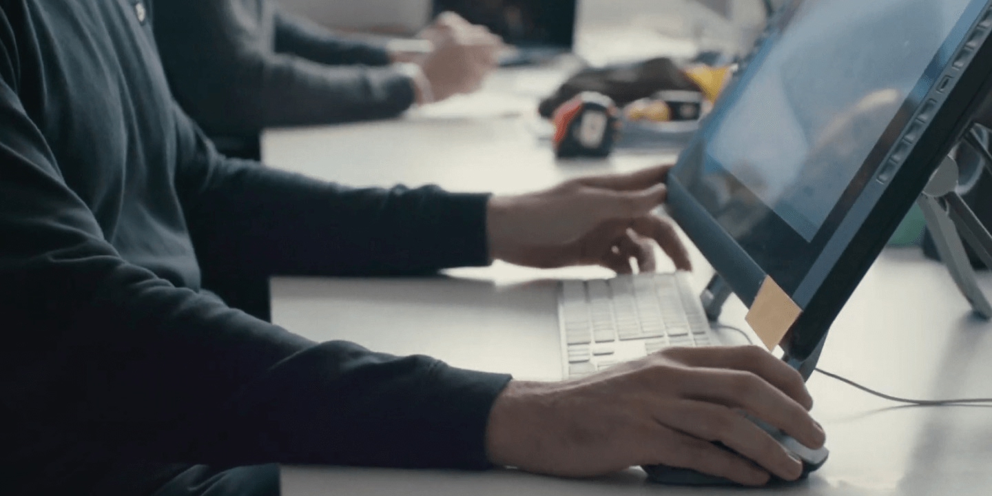 Multiple professionals collaborating around white work table with laptops, keyboards, and measurement tools, demonstrating team collaboration with digital and physical tools in professional workspace environment.