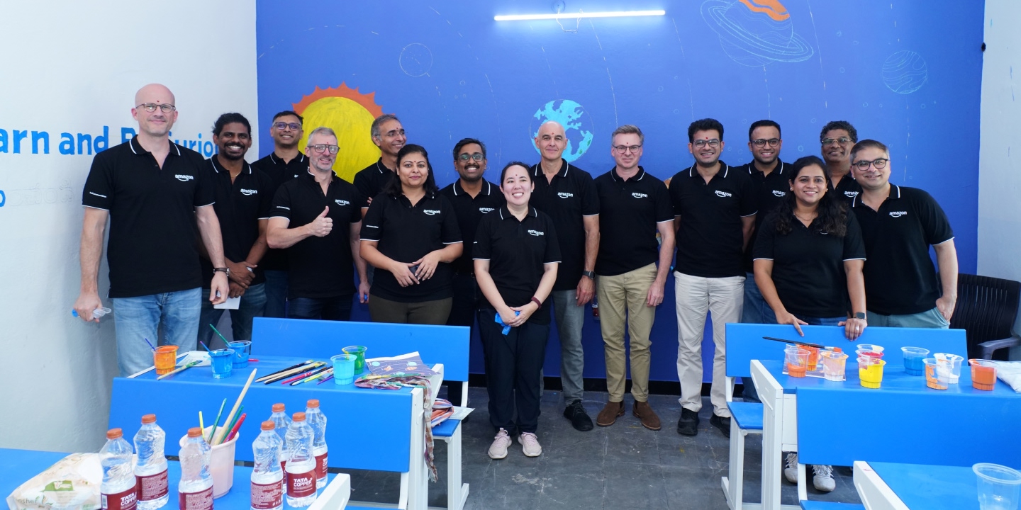A group of Amazon employees pose for a photo in front of a mural.