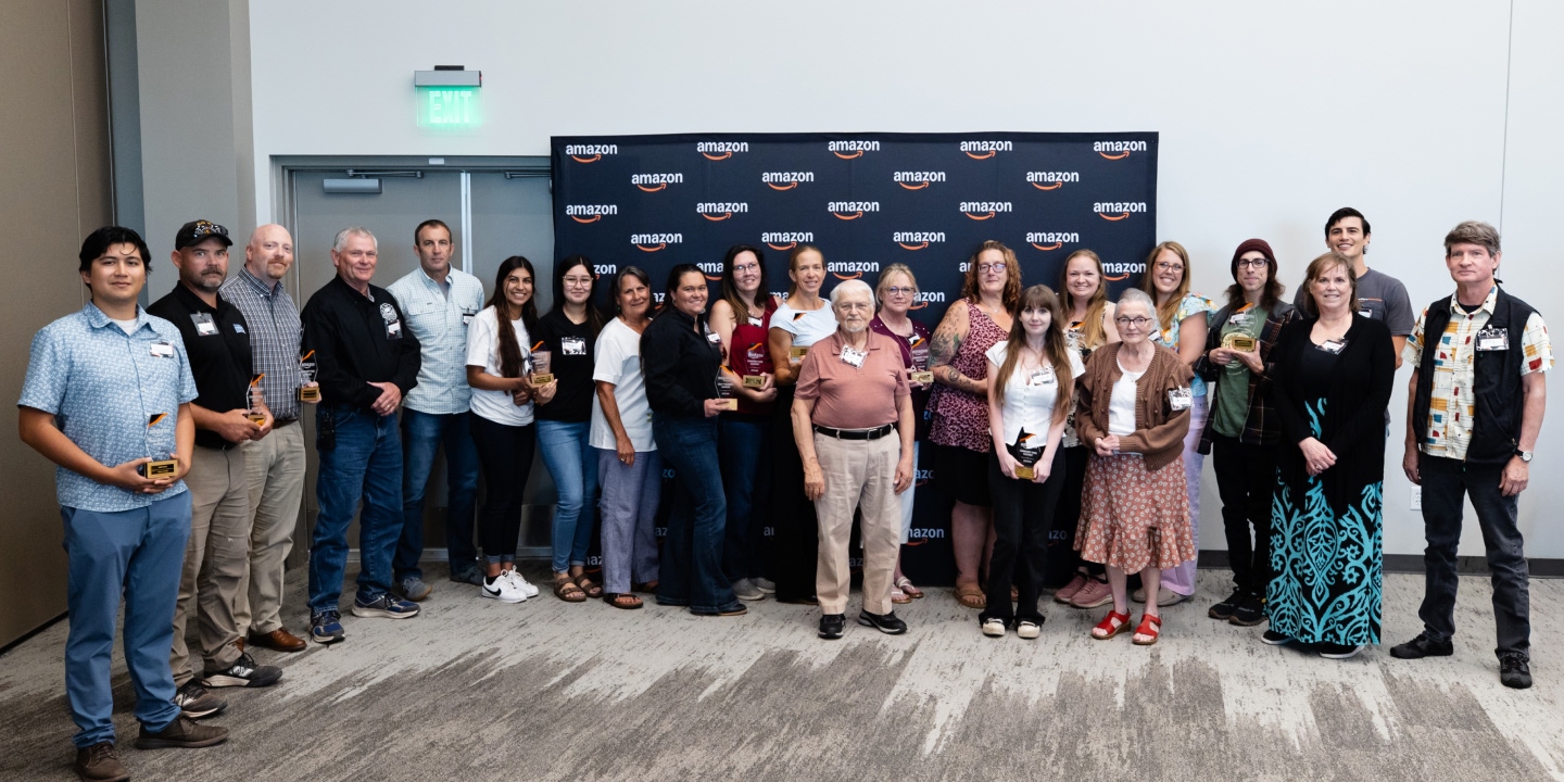 A group of people standing in front of a wall with Amazon logos and holding trophies.