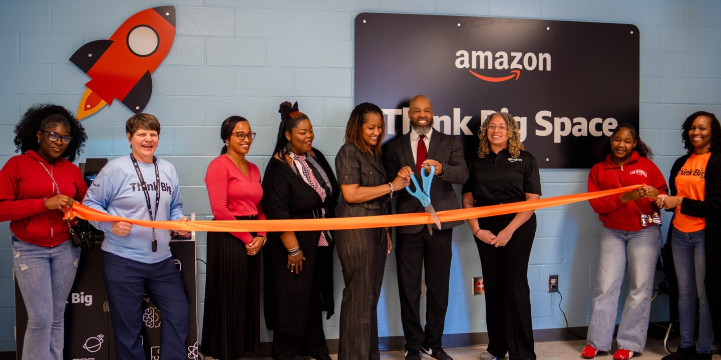 A group of eight people cut a ribbon at the opening of an Amazon Thinking Space.