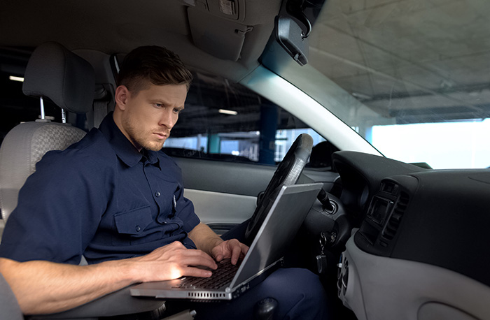 Male police officer working on laptop in car, filling data in crime report