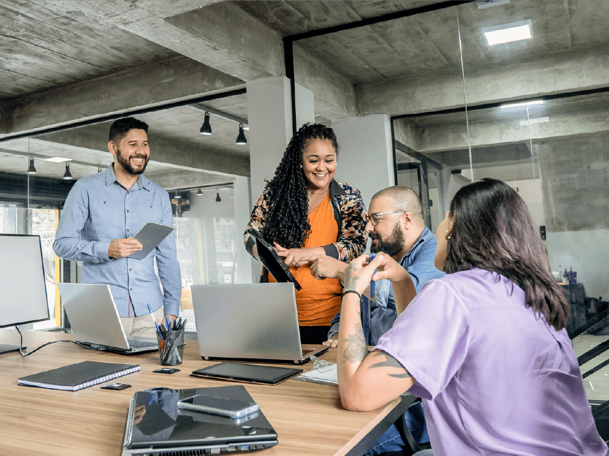 office workers sitting at long desk with laptops in discussion